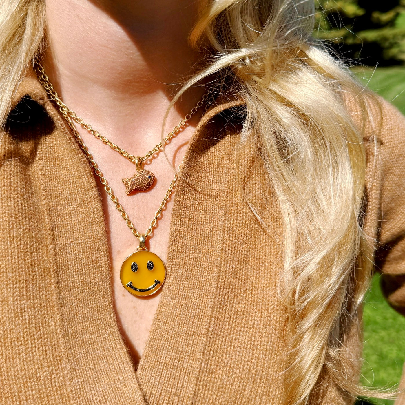Person wearing a gold necklace with a smiley face pendant outdoors