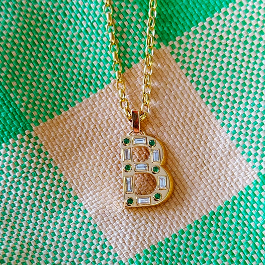 Pendant with gemstones in the shape of a letter B and gold chain on green and off-white checkered fabric