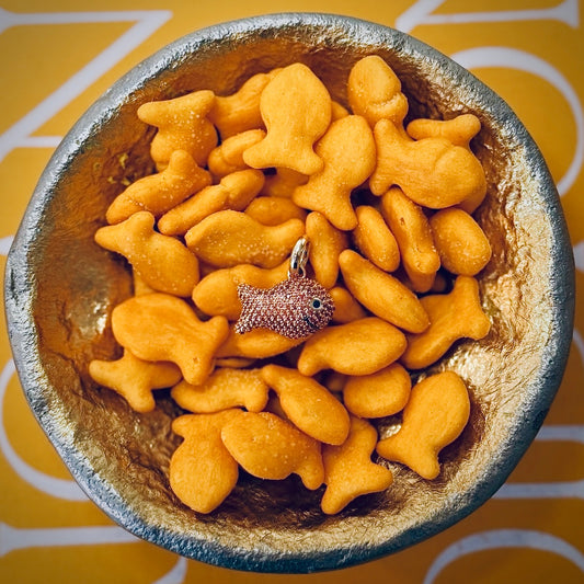 Bowl of goldfish crackers with a goldfish-shaped charm on a yellow and white patterned background