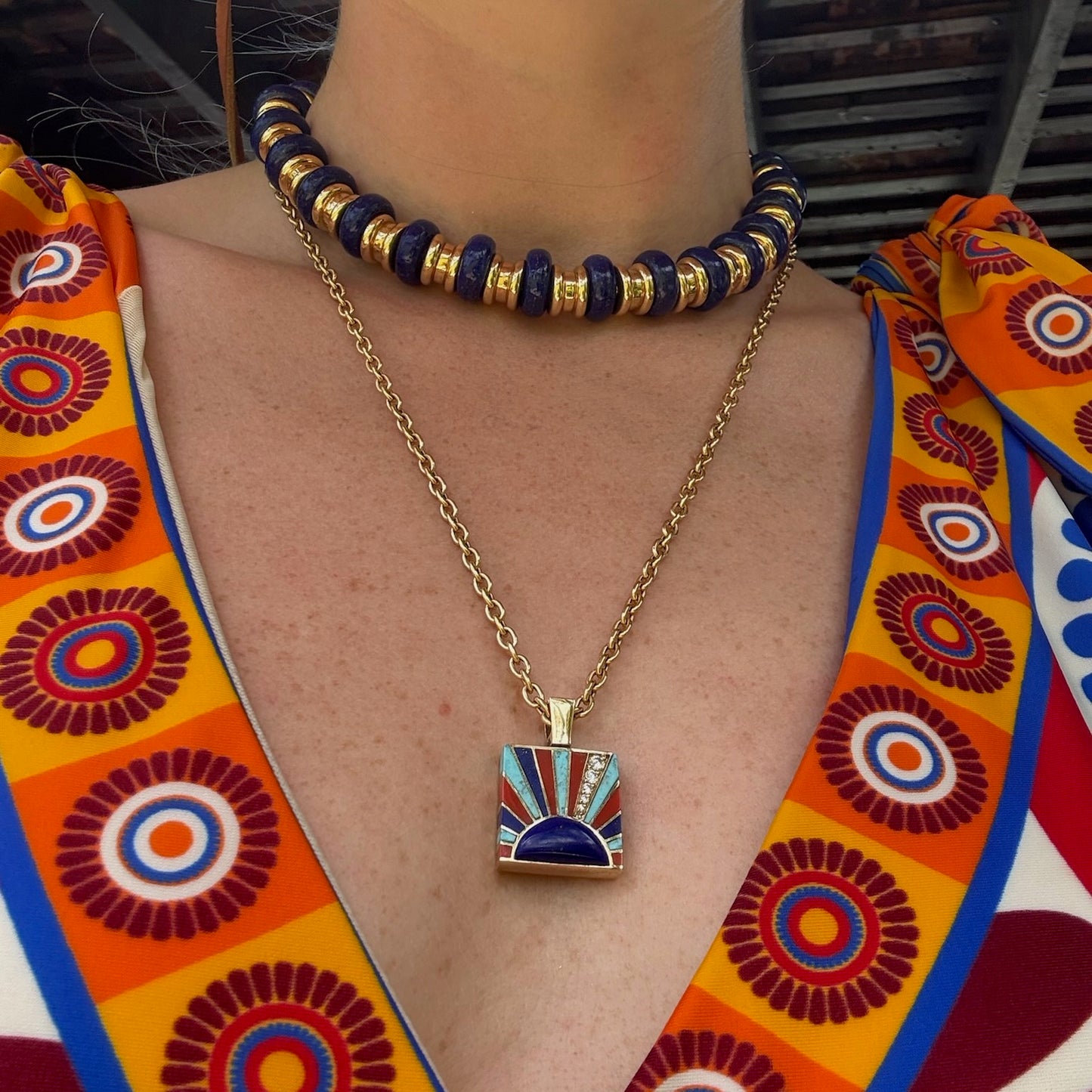 Necklace with a colorful pendant worn by a person with a patterned garment.