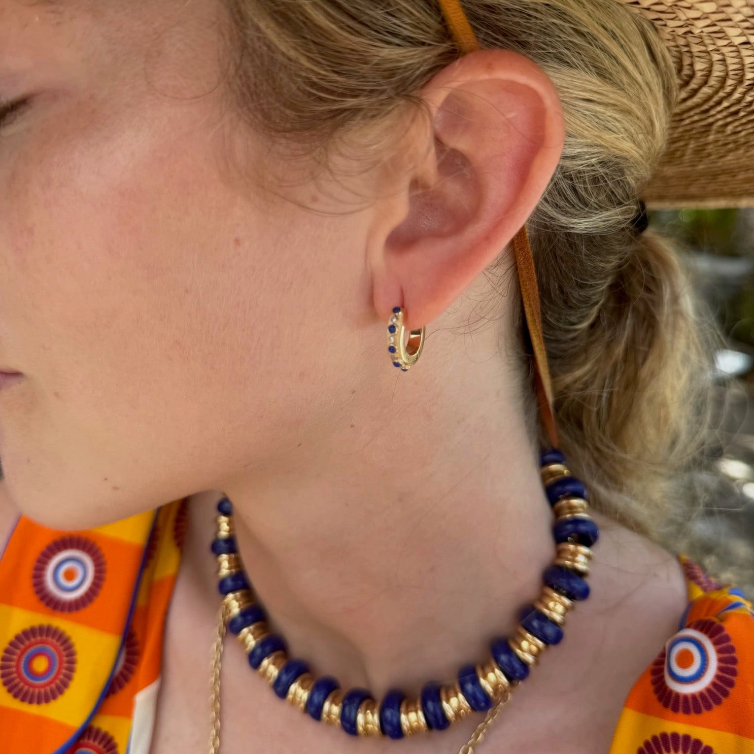 Close-up of a person wearing a blue and gold beaded necklace and hoop earrings.