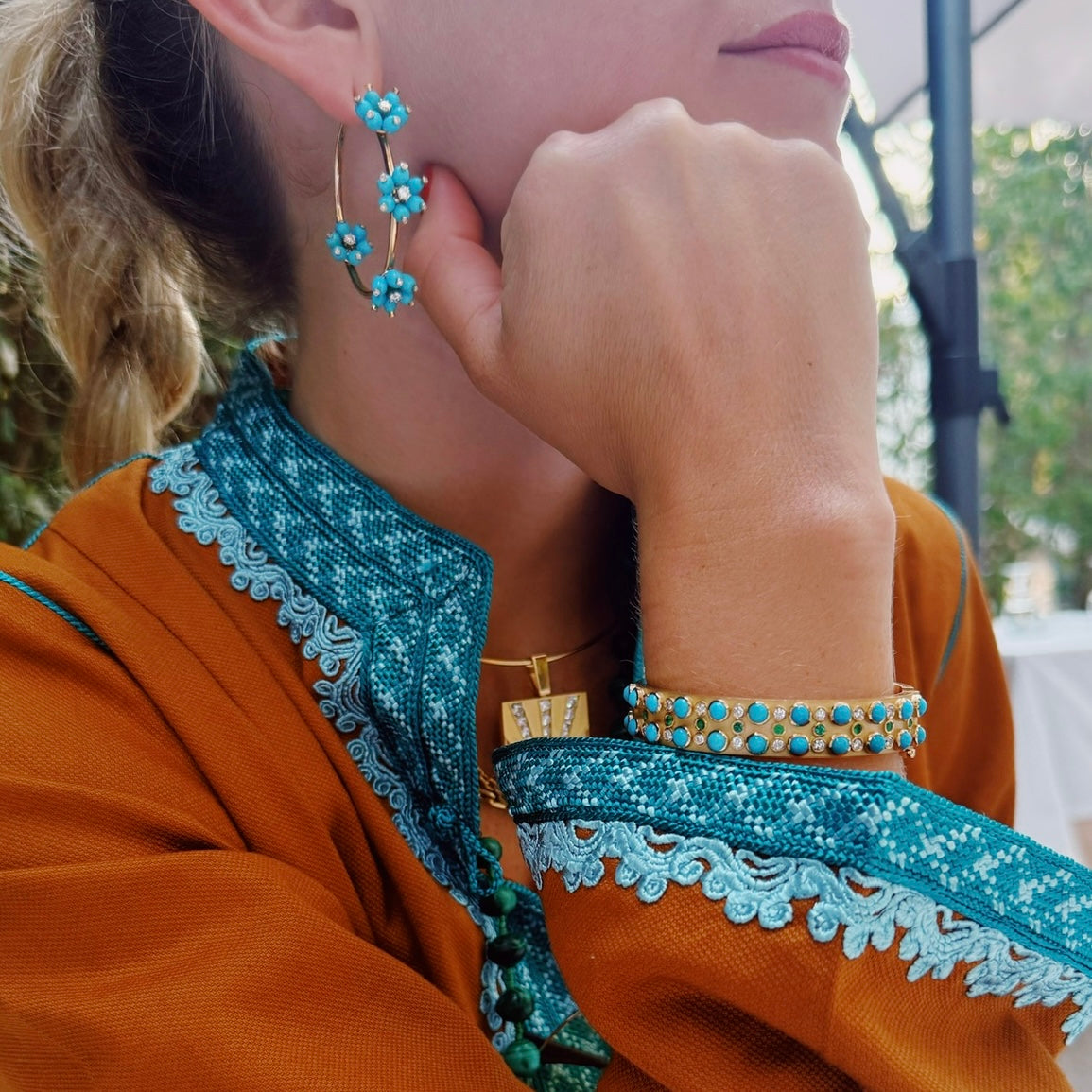 Close-up of a person wearing turquoise floral earrings and bracelets, with a blurred background.