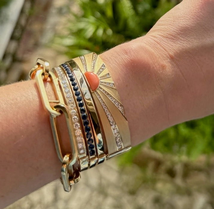 Close-up of a wrist wearing multiple gold bracelets with a blurred natural background