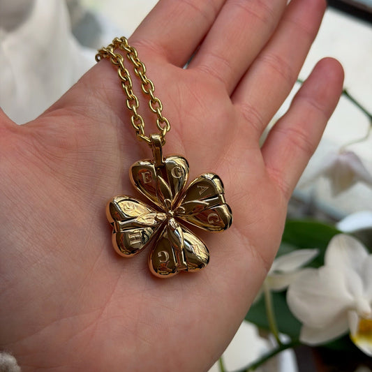 Gold four-leaf clover pendant on a chain held in a hand with a blurred floral background