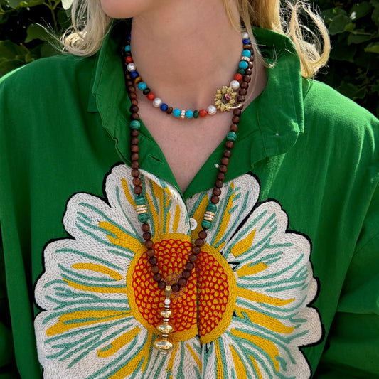 Woman wearing a green shirt with a large embroidered flower design, colorful beaded necklace, and earrings.