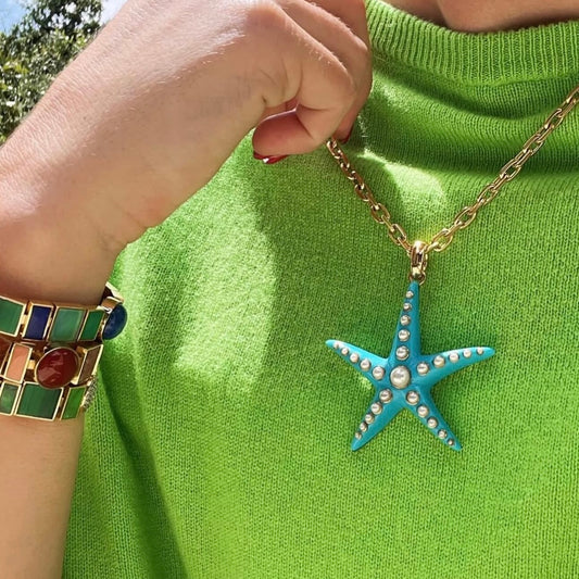 Starfish pendant necklace on a green sweater with a hand wearing a bracelet.
