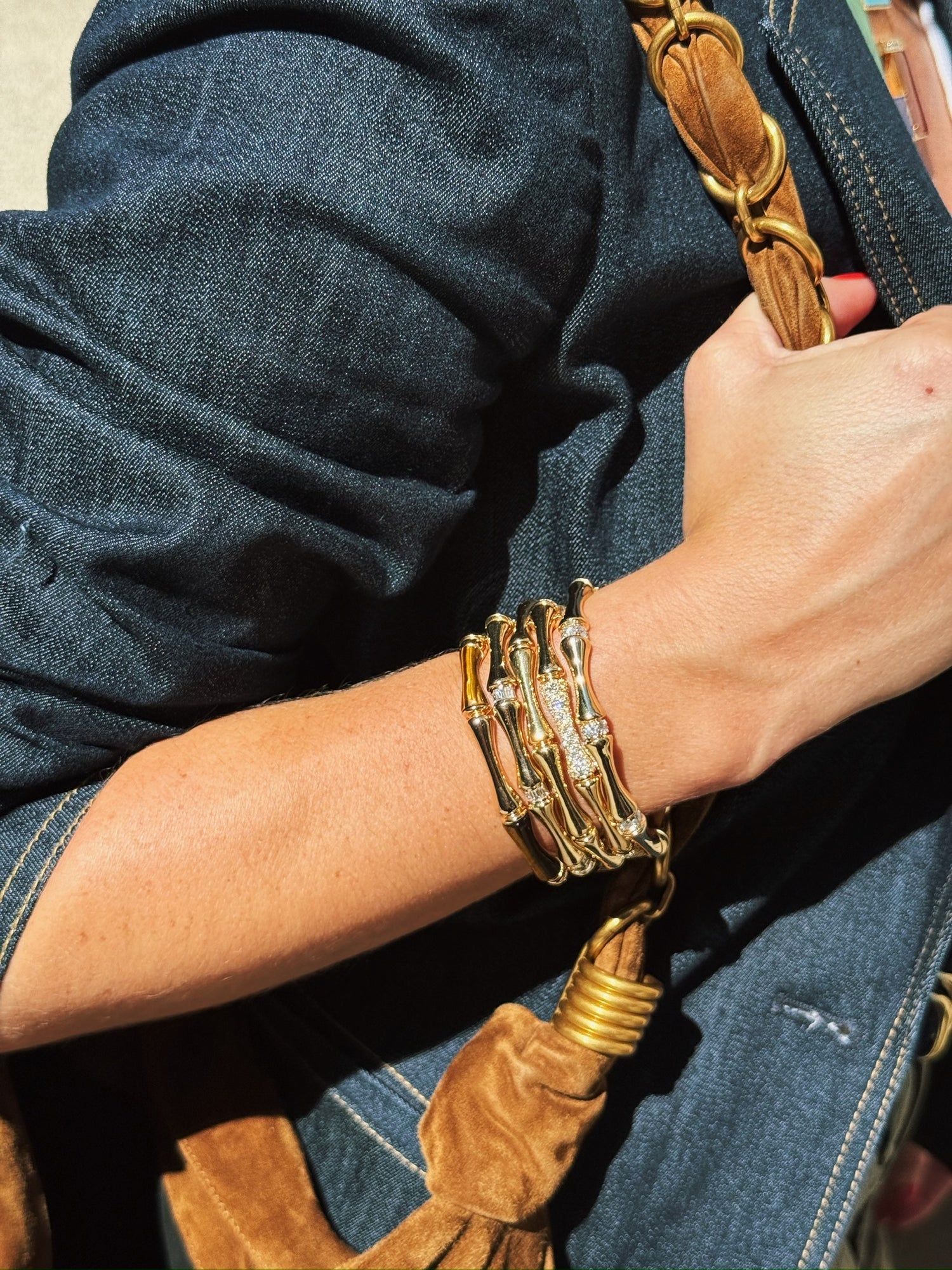 Close-up of a person wearing gold bracelets on a brown leather strap.