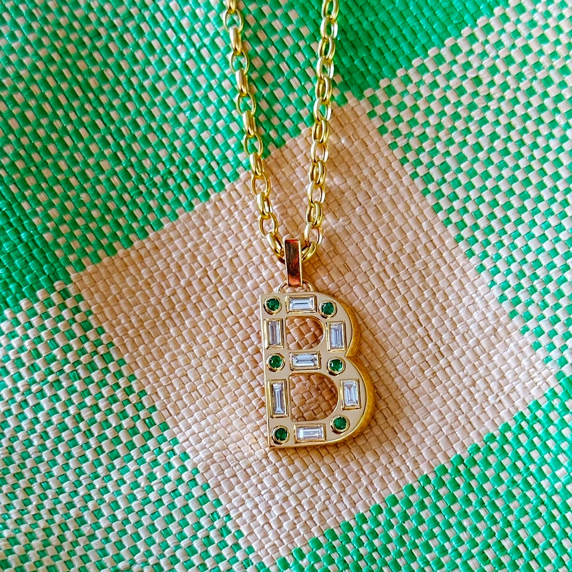 Pendant with gemstones in the shape of a letter B and gold chain on green and off-white checkered fabric