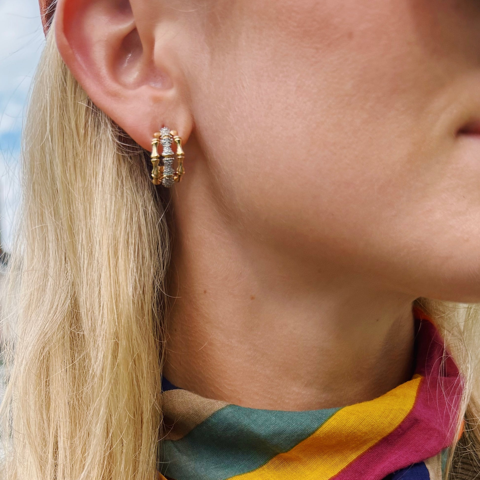 Close-up of a person wearing gold hoop earrings with a blurred background