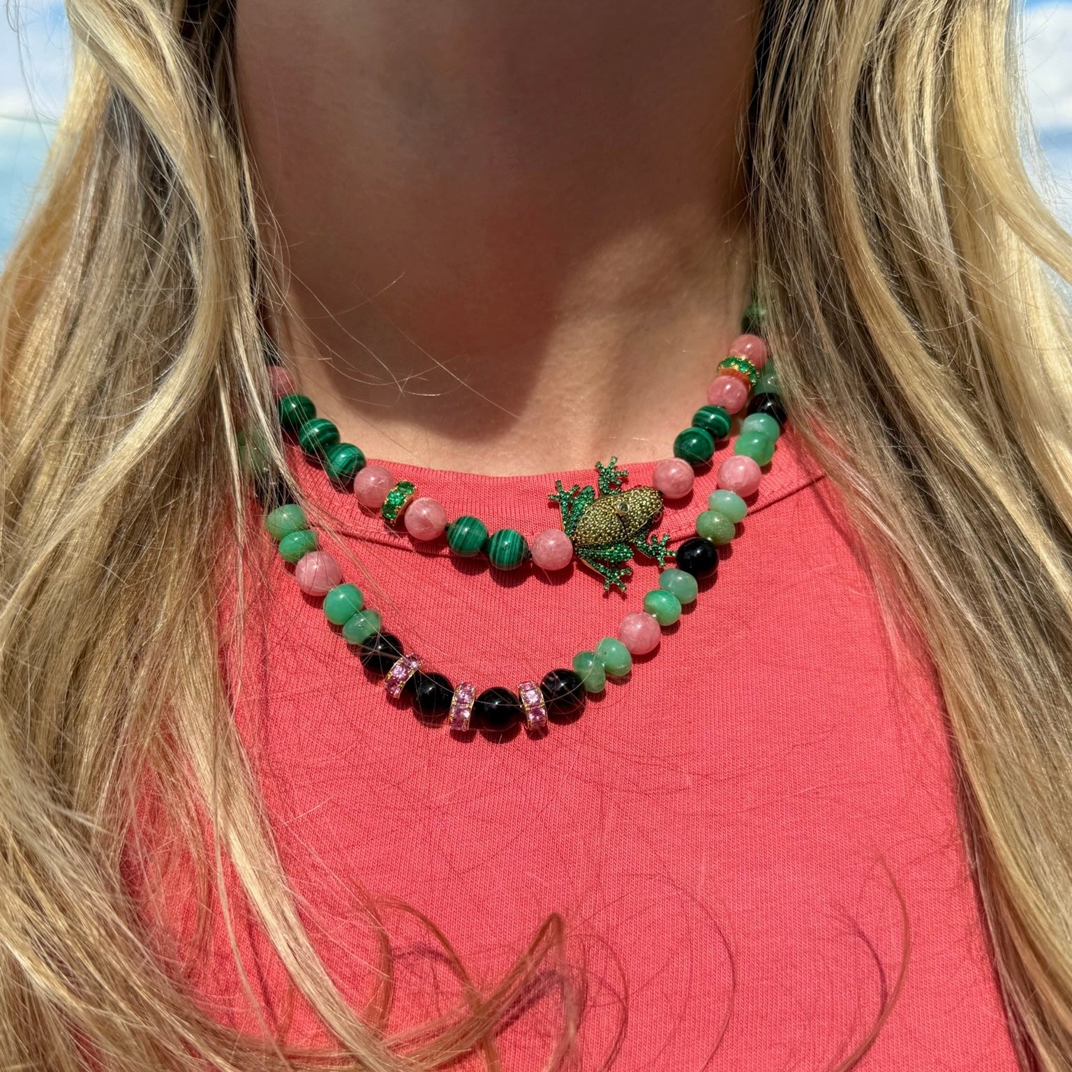 Necklace with green, pink, and black beads on a person wearing a red top.