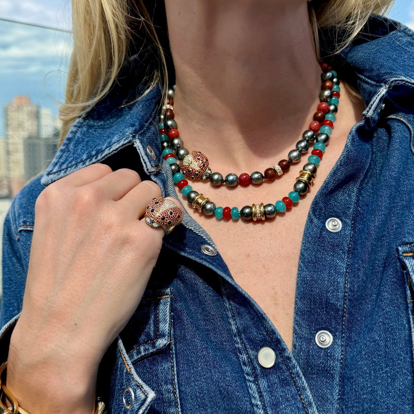 Person wearing a colorful beaded necklace and denim jacket with a cityscape in the background