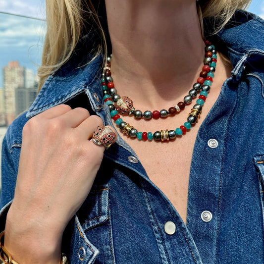 Person wearing a colorful beaded necklace and denim jacket with a cityscape in the background