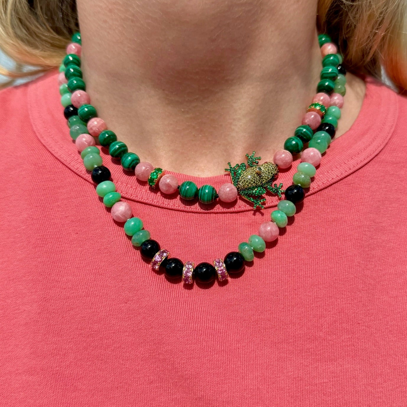 Necklace with green, pink, and black beads worn by a person on a pink shirt