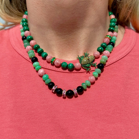 Necklace with green, pink, and black beads worn by a person on a pink shirt