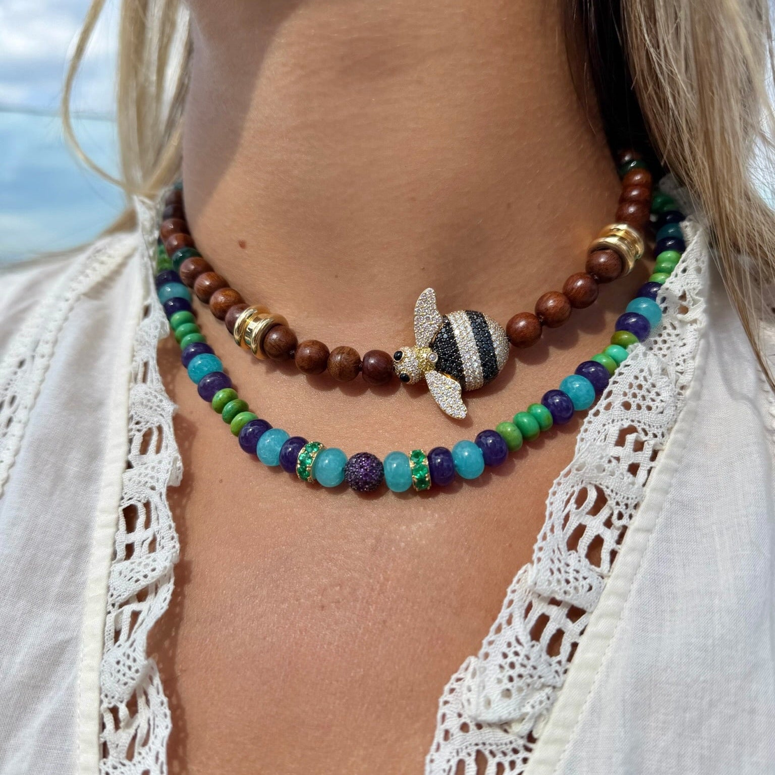 Close-up of a person wearing a colorful beaded necklace with a butterfly charm against a blurred natural background.