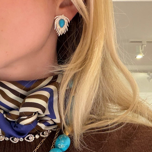 Person wearing a colorful necklace with a large pendant, brown sweater, and striped scarf.