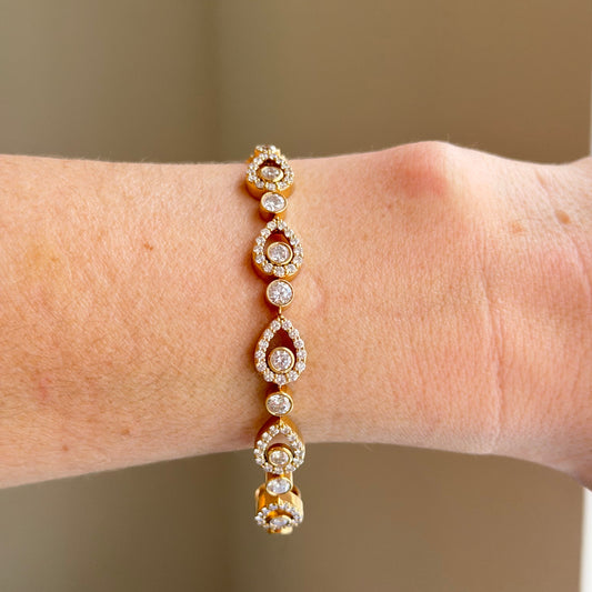 Gold bracelet with gemstones on a wrist against a neutral background