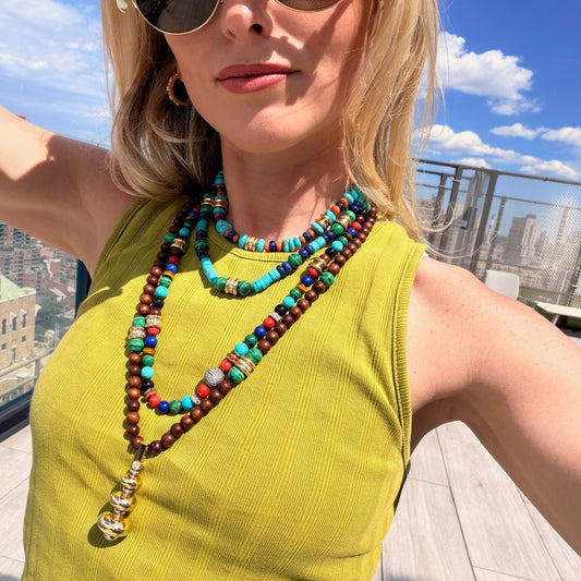 Woman wearing sunglasses and a colorful beaded necklace on a rooftop with a cityscape in the background.