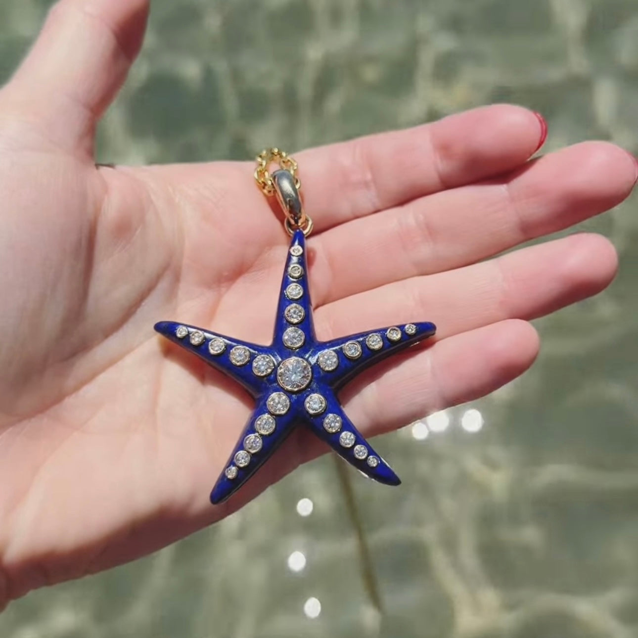Blue starfish pendant with rhinestones held in a hand by a body of water.