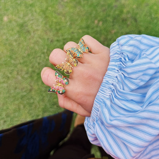 Hand wearing colorful butterfly rings with a blurred green background