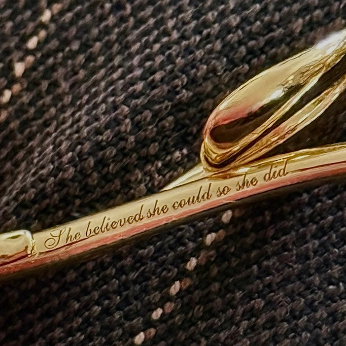 Gold jewelry with engraved text on a textured brown background