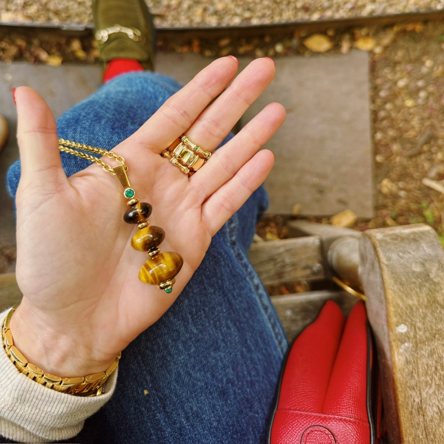 Hand wearing gold jewelry with a necklace and rings, outdoors.