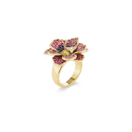 A gold ring shaped like a flower, featuring pink pavé-set petals, a black center stone, and a yellow center stone, shown on a plain white background.