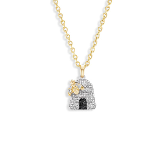 A gold chain necklace with a beehive-shaped pendant paved with clear stones, featuring a small gold bee and a black arched doorway, shown on a plain white background.